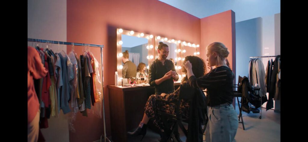 Make-up-Artist Bülent Muşdu bei der professionellen Vorbereitung eines Models vor einem beleuchteten Schminkspiegel während eines Videodrehs für HSE24.